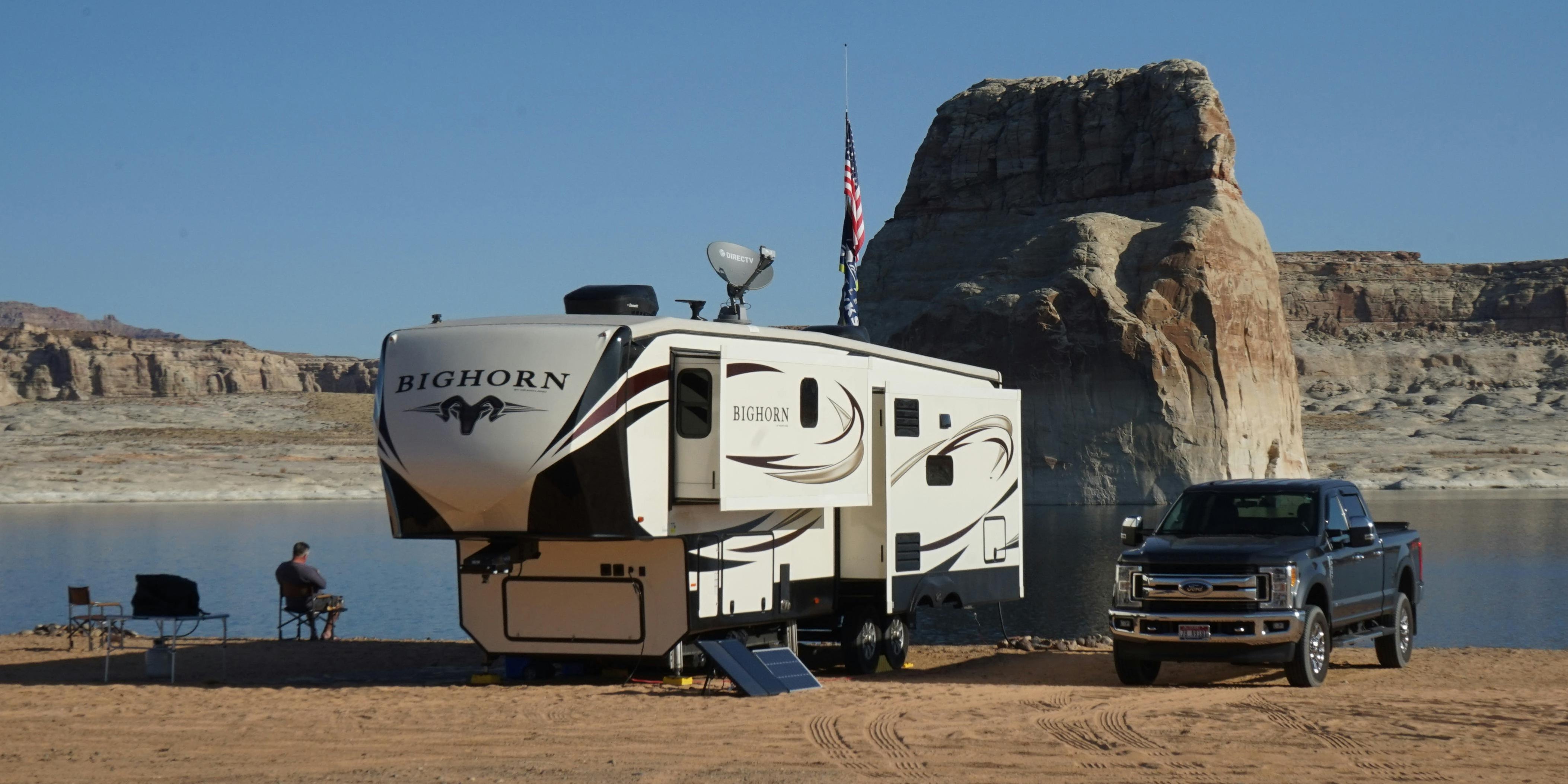 RV 5th wheel by the lake with 2 A/C units on the roof and a pick up track next to it